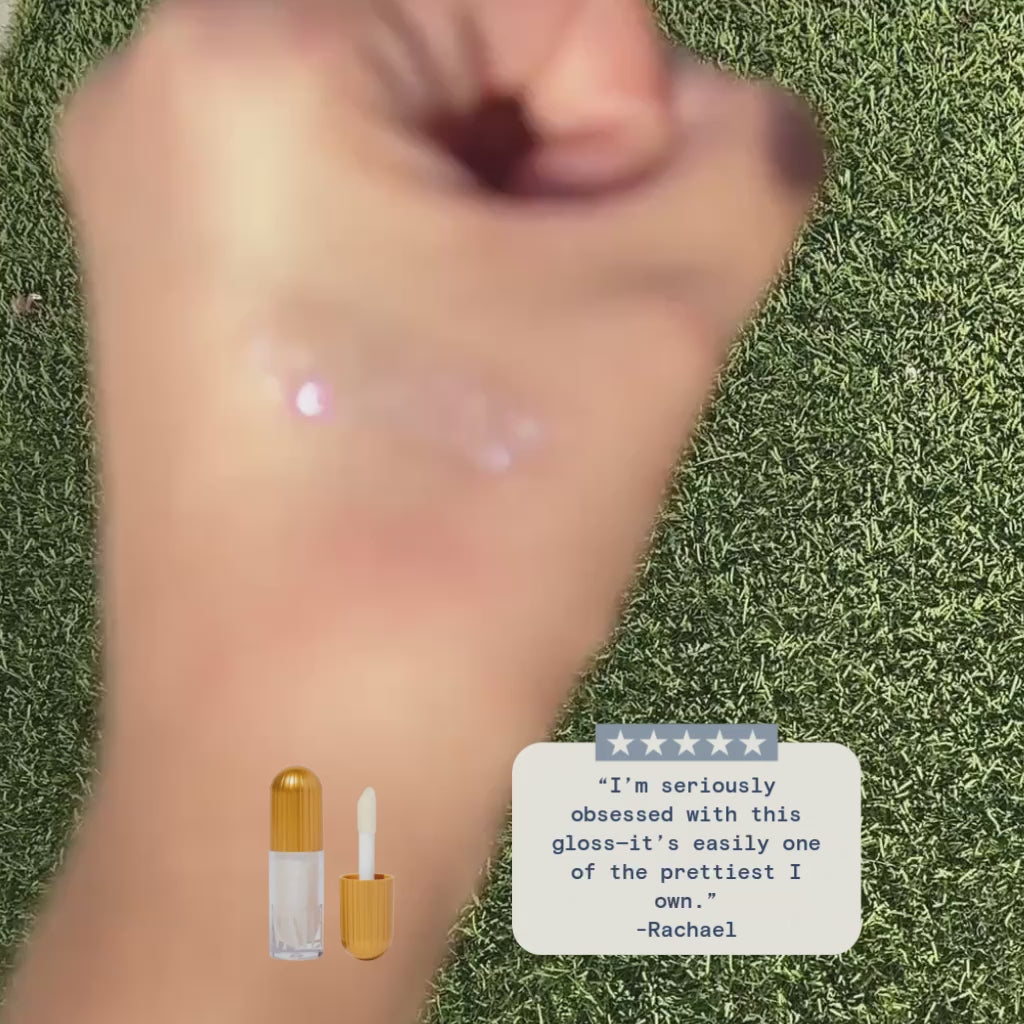 a blurred hand with a grassy background showing the sparkle effect of the aileen lipgloss, towards the end of the video it focuses on the hand to show a better look at the sparkly gloss