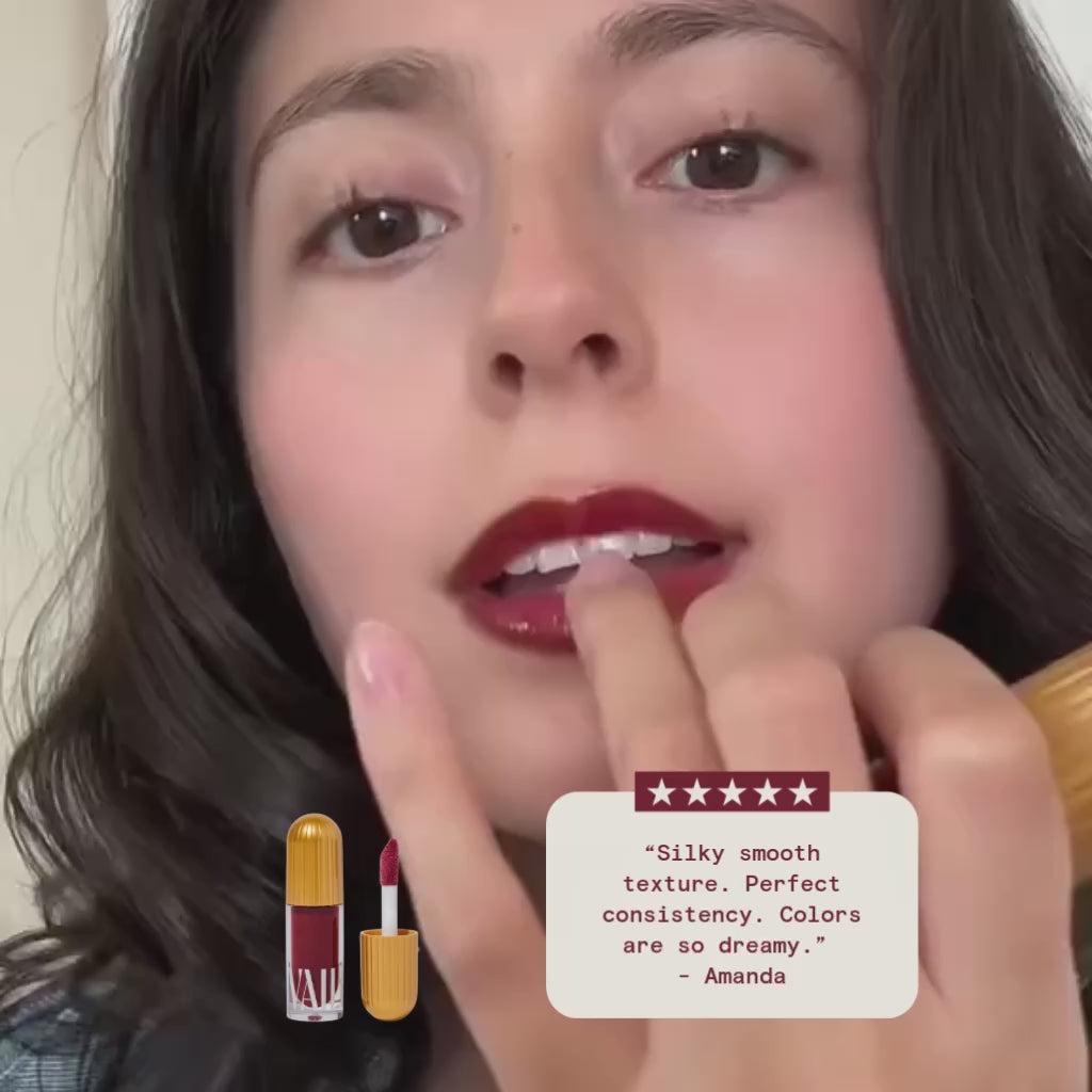 A woman shows the lipgloss shade guadalupe on her lips with a review on display that says "silky smooth texture.colors are so dreamy." by Amanda